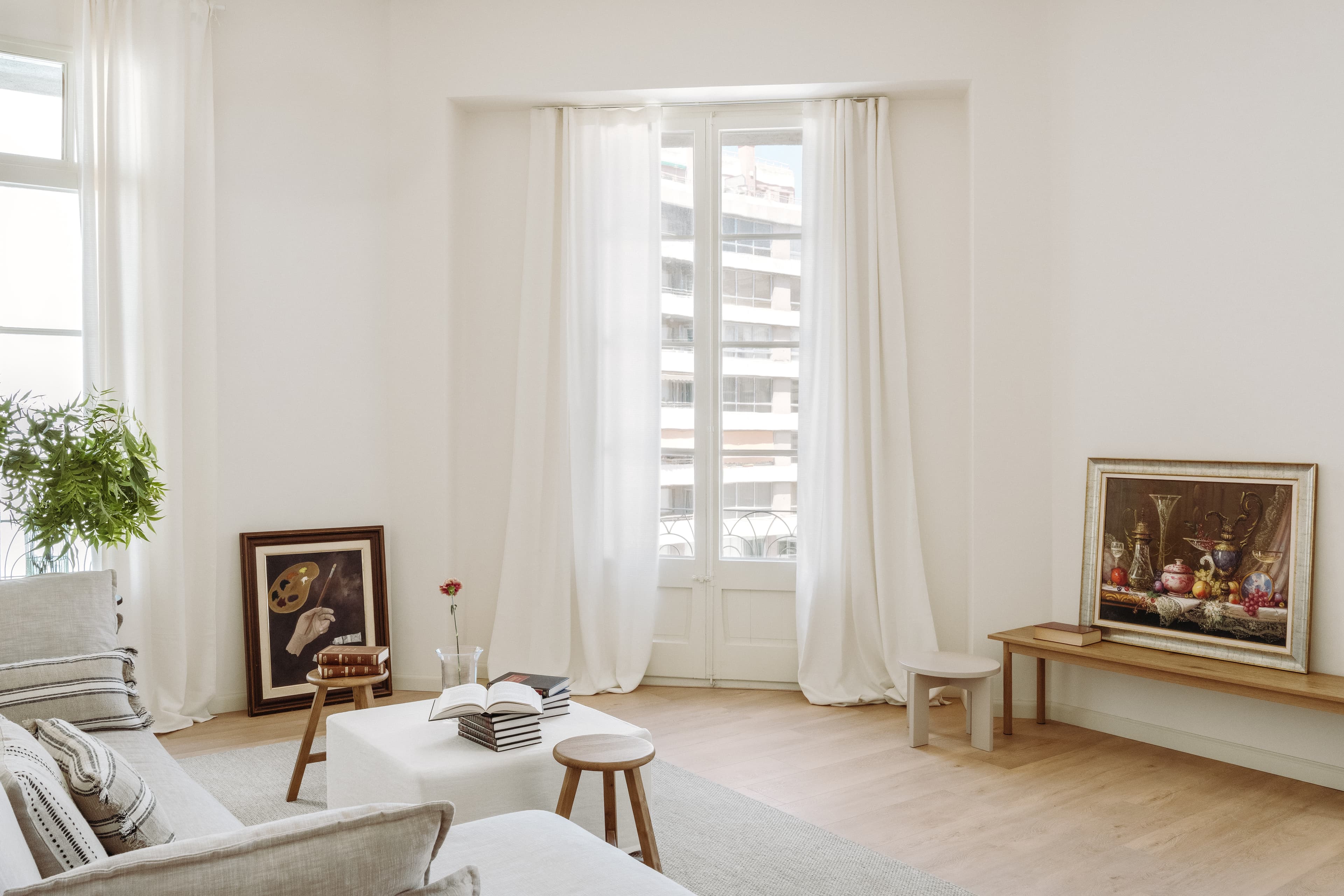 Vista del salón el lateral del sofá, con las cortinas y ventanas al fondo