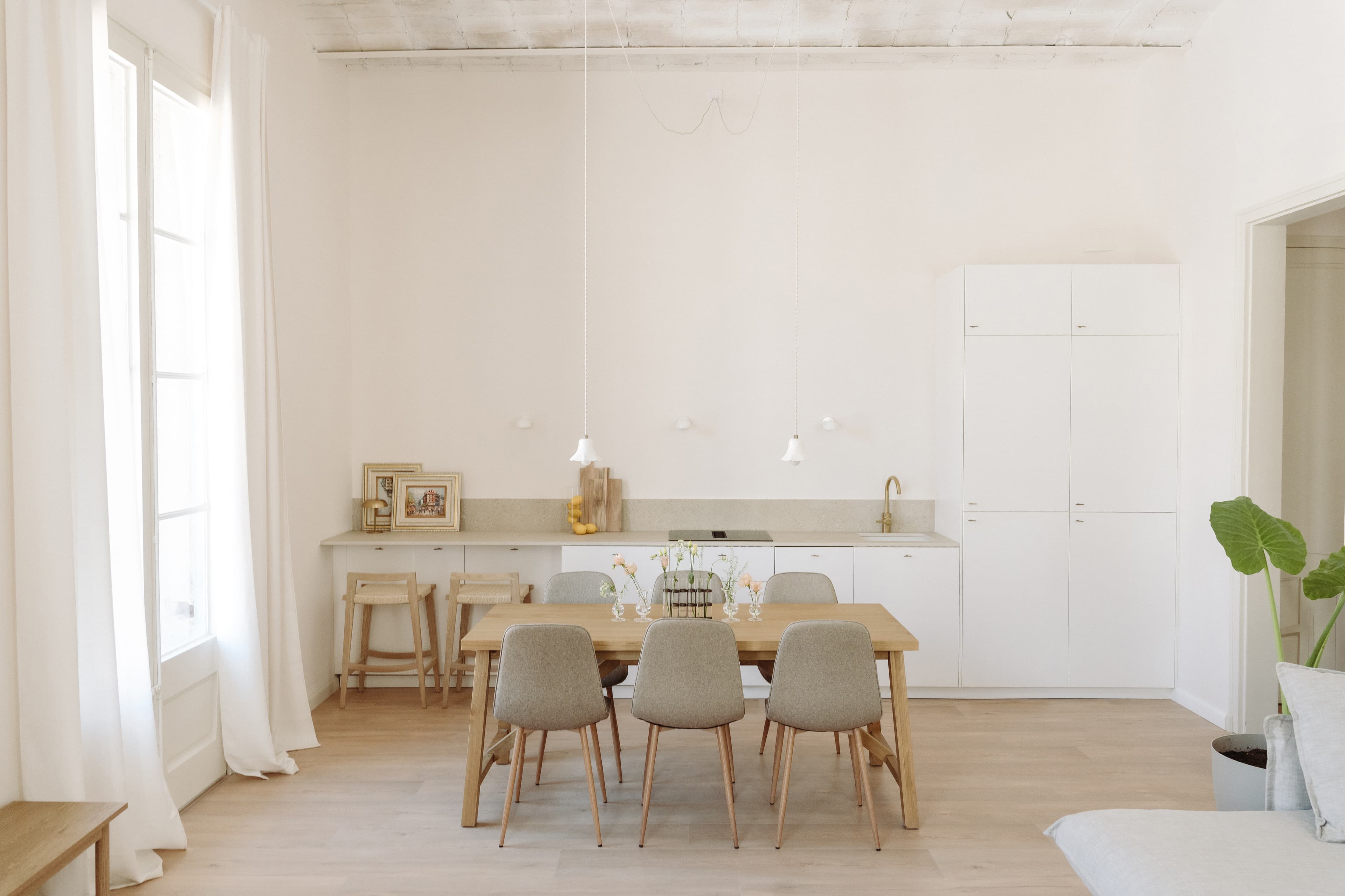 Mesa de comedor con sillas y lámpara colgante, con cocina al fondo